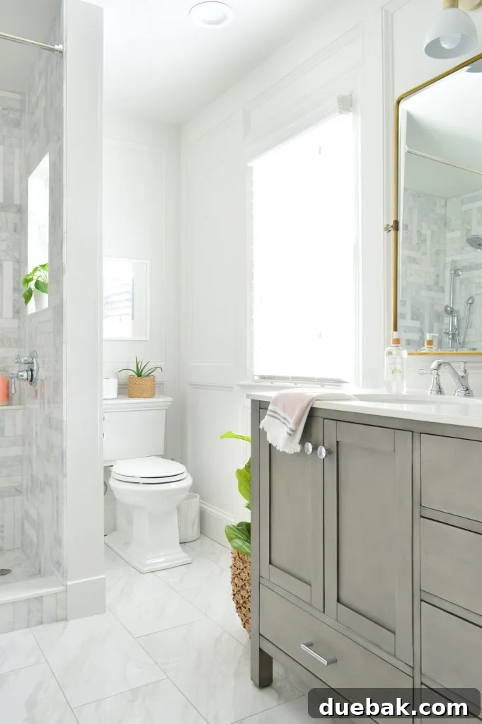 View of the Kohler Memoirs toilet in the back corner of a marble bathroom with a stylish gray vanity