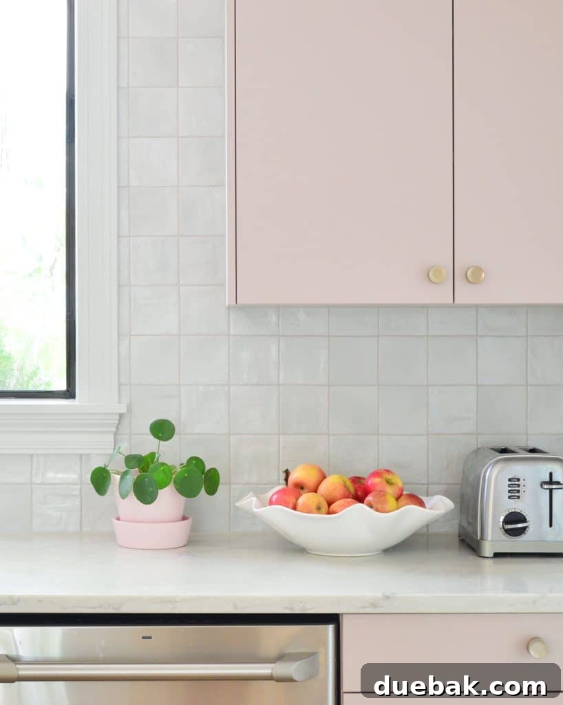 Stylish kitchen with mauve pink painted cabinets, square zellige-style tile backsplash, and minimalist decor.
