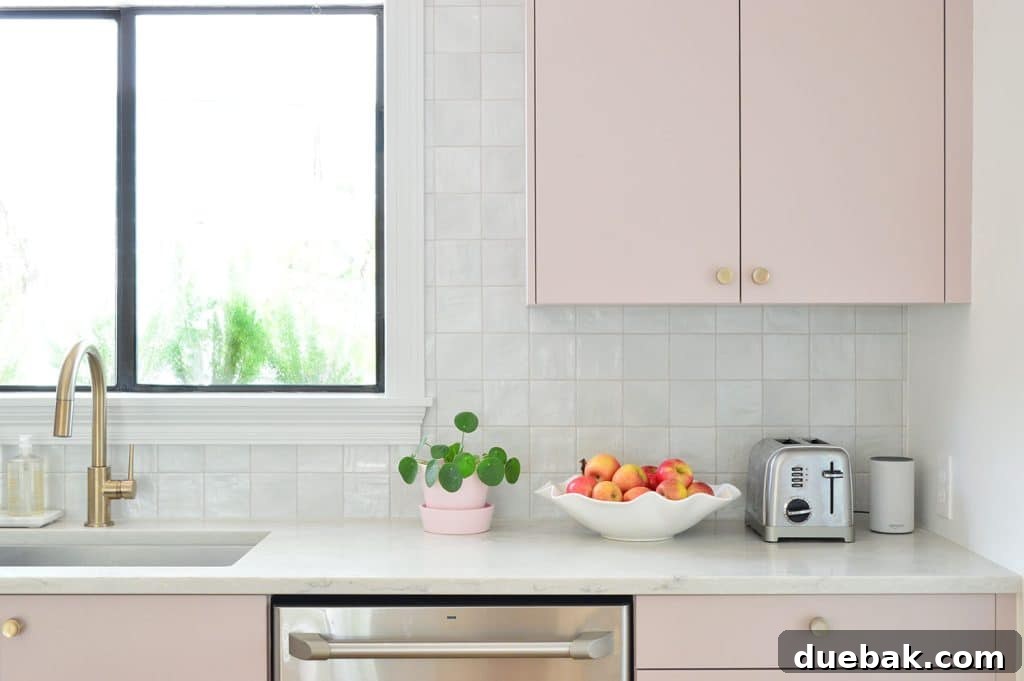 Close-up of square tile backsplash with mauve pink painted cabinets and brass hardware, highlighting texture and color.