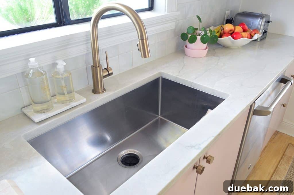 Deep stainless steel sink and gray natural quartz countertops with a modern brass faucet, showcasing practicality and style.