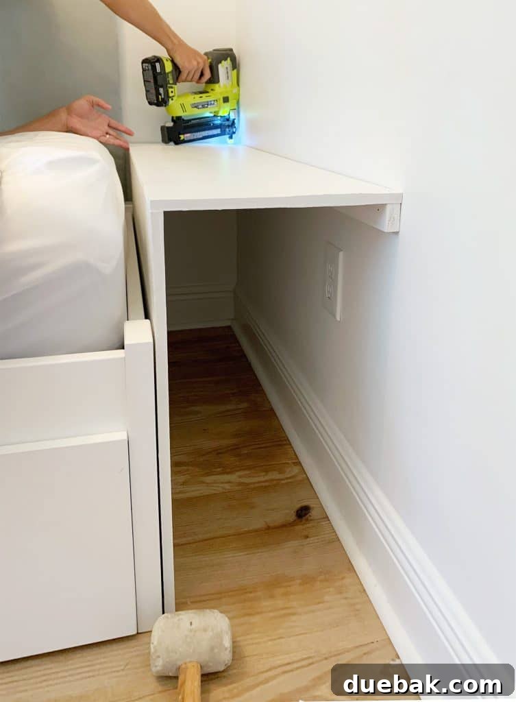 Detail shot of painted MDF pieces being meticulously nailed into place for the bottom shelf of the built-in bookcase, demonstrating secure and precise assembly during the DIY process.