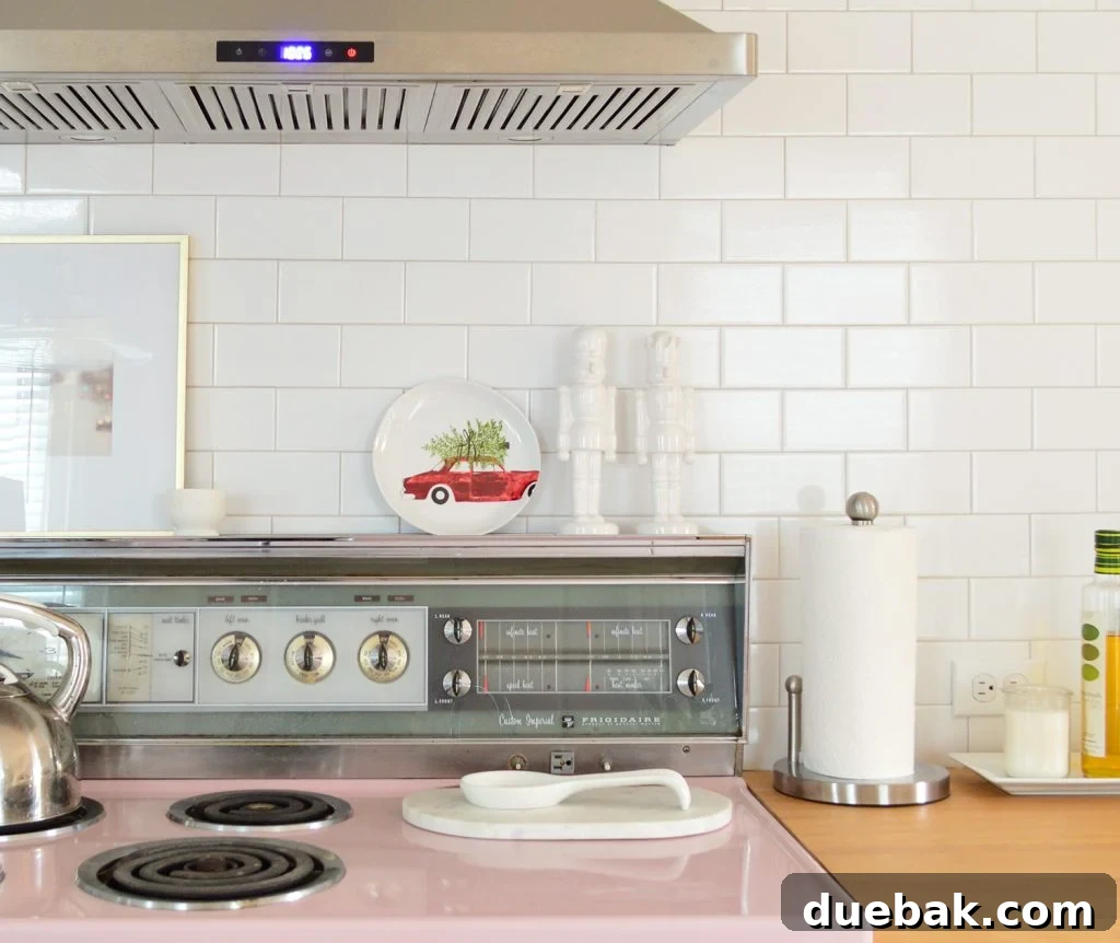 A retro pink stove in a kitchen with classic white subway tile, adorned with a festive Christmas plate, creating a charming and whimsical holiday setting.