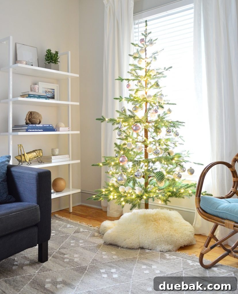 A sparse, pre-lit faux fir Christmas tree stands beside a modern bookshelf, offering a charming and minimalist holiday display.