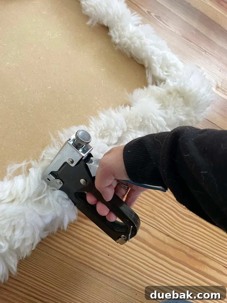Sherry diligently stapling an old sheepskin rug around the MDF base, transforming it into a cozy upholstered loveseat seat, showcasing the DIY process.