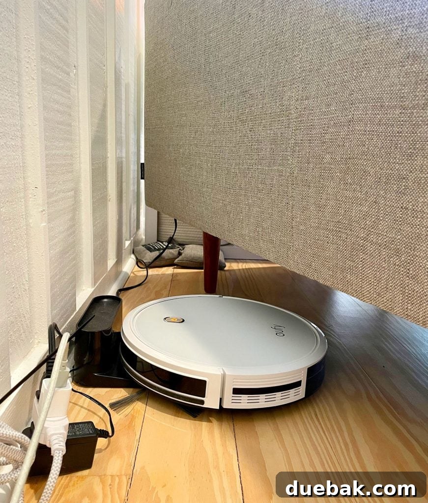 Eufy RoboVac 11S Max charging at its base station, cleverly plugged in and hidden under a couch
