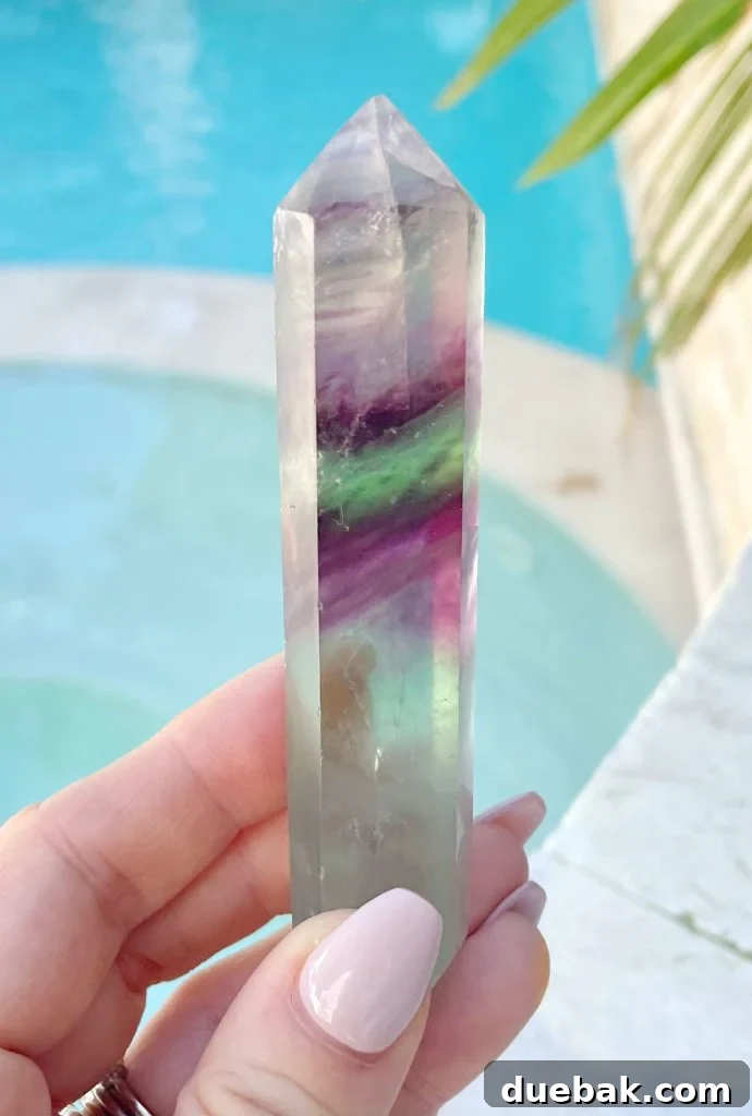 Rainbow Fluorite: Unlocking Its Energy and Purpose 2 Rainbow Fluorite Crystal Point In Hand By Pool, showcasing its vibrant purple, blue, and green banding under natural light.