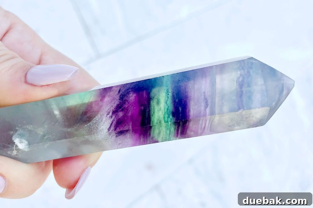 Rainbow Fluorite: Unlocking Its Energy and Purpose 4 Hand holding crystal with purple green rainbow banding, showcasing its unique patterns and clarity.