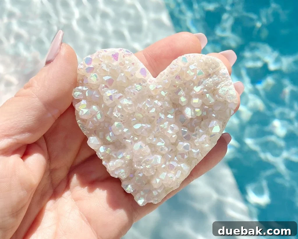 A hand gently cradling a heart-shaped Rainbow Angel Aura Quartz gemstone, shimmering with iridescent colors.