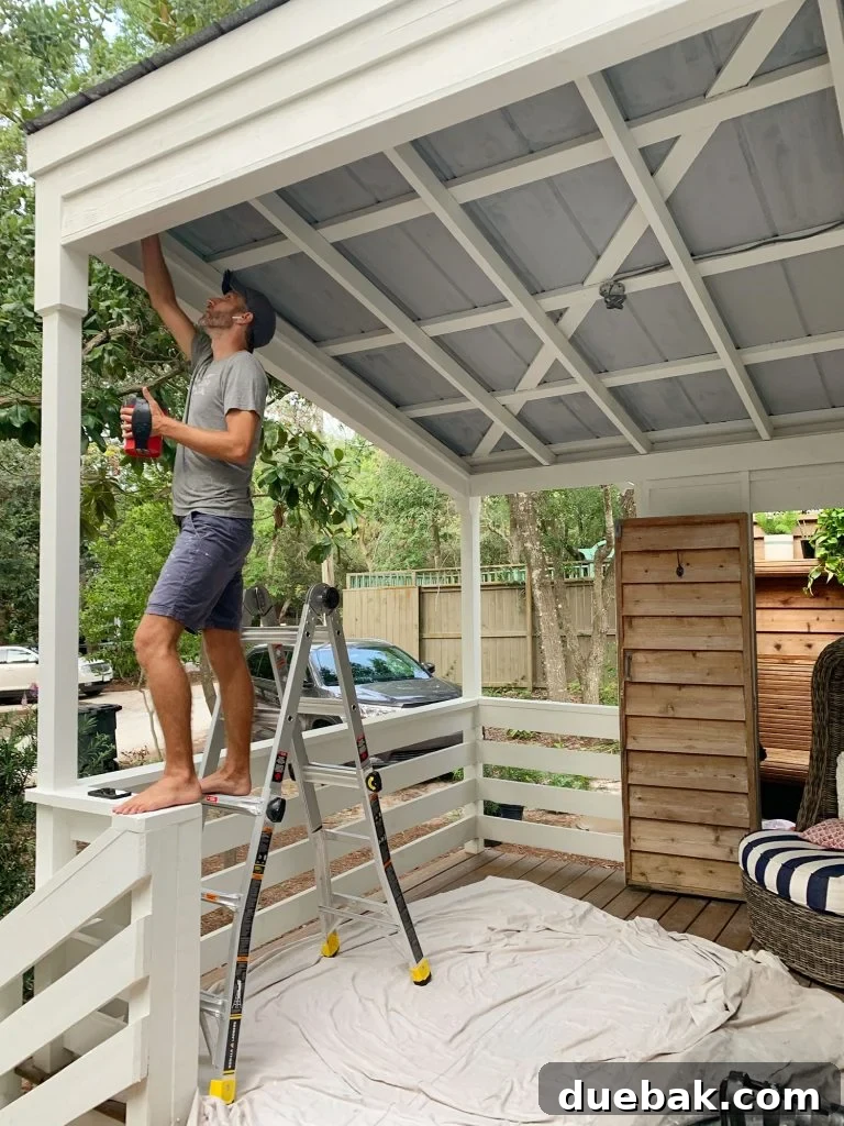 Southern Serenity: Top Haint Blue Paint Shades 12 John Standing On Ladder Priming Metal Porch Ceiling, demonstrating preparation steps for painting.