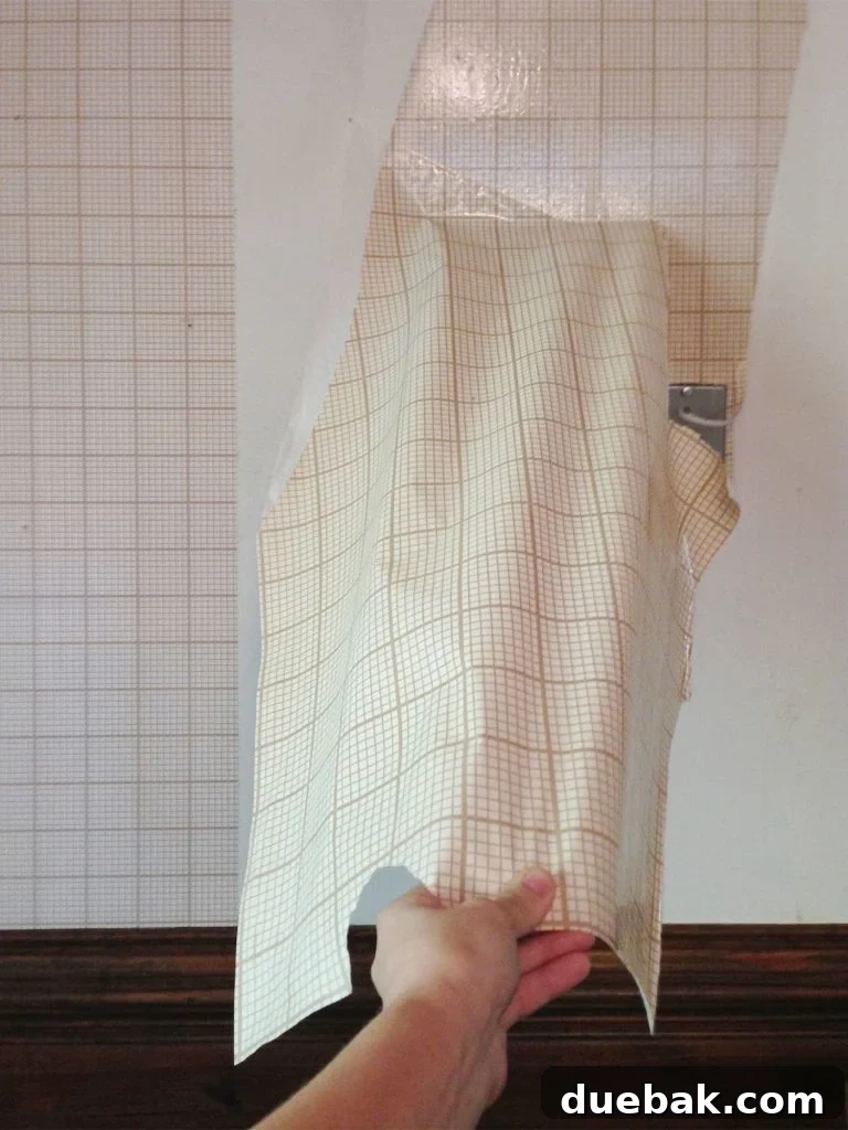 Hand peeling off large section of gridded wallpaper