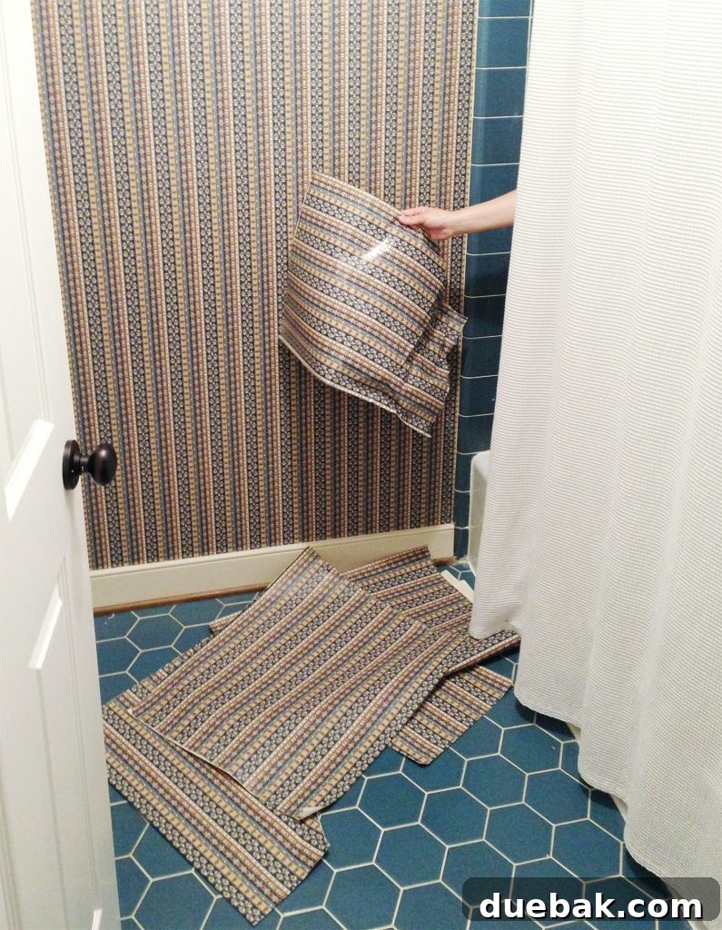 Hand removing wallpaper from shower in blue bathroom