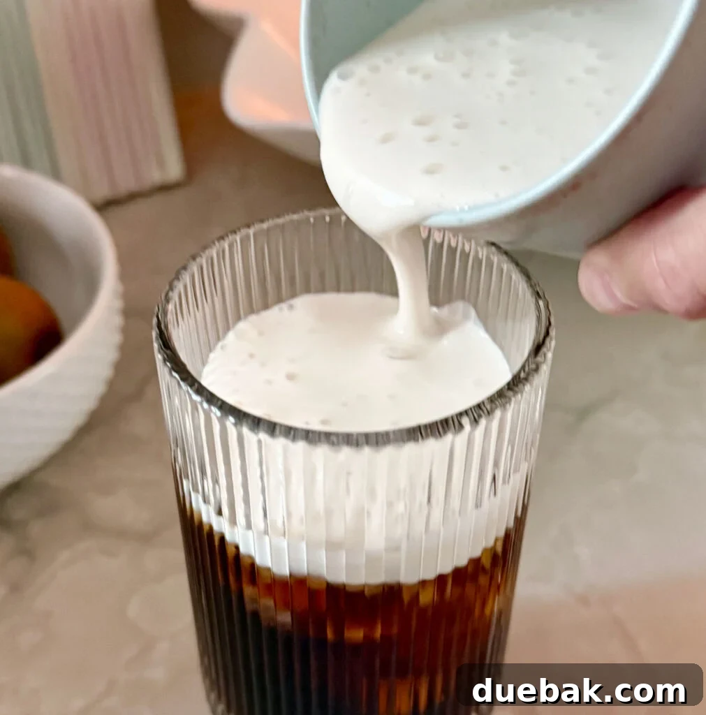 Brew Your Own Perfect Cold Brew 12 Pouring homemade cold foam creamer over cold brew coffee