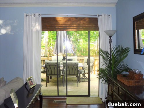 sliding doors treated like window with white curtains on either side and wood blind above