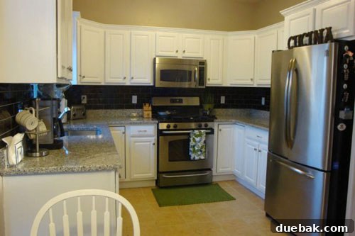 Transform Your Kitchen with Painted Wood Cabinets 5 After kitchen view showing white cabinets, green curtains, and modern decor