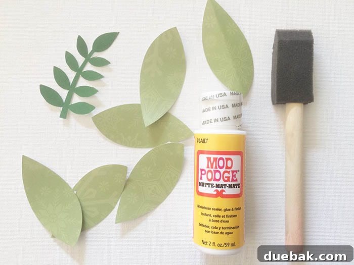 Close-up of a hand applying Mod Podge to a paper leaf with a foam brush