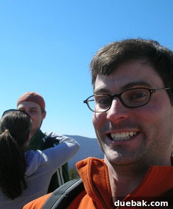John's cousin Travis smiling playfully, with Sherry and John kissing in the background after their engagement.
