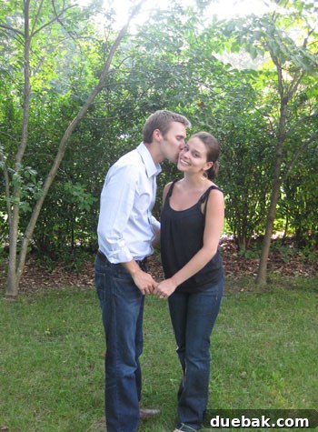 A couple posing romantically in front of lush green hedges in their backyard, a sentimental spot reminiscent of their wedding day family portraits, for their anniversary pictures.