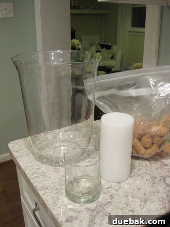 The Secret to Straight Candlesticks 4 Supplies laid out for a DIY cork centerpiece: hurricane vase, pillar candle, juice glass, and a bag of wine corks