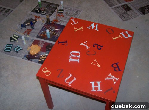 DIY Kids' Furniture: Vibrant Paint Makeover 3 Jennifer's IKEA kids table in mid-transformation, painted red with various colorful alphabet stamps applied, showing foam stamps nearby.
