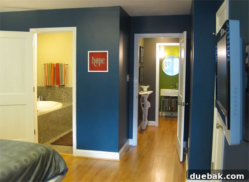 Interior view from an inky blue bedroom revealing a vibrant green room beyond, showcasing a sophisticated layered color design with crisp white accents and a stylish hallway table