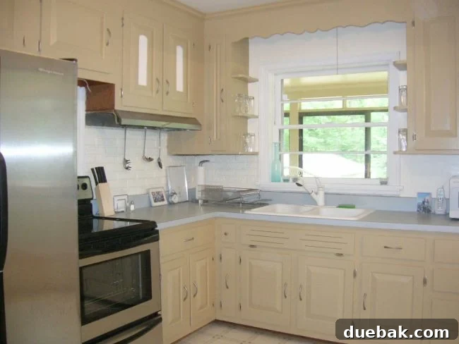 Kitchen after initial cosmetic updates: new paint on cabinets, modern stainless steel appliances, and updated hardware, showing a brighter, more contemporary look.