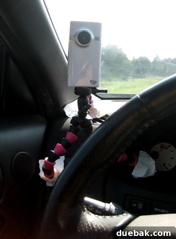 Close-up of a homemade dashboard camera setup, featuring a camera mounted on a tripod secured with white duct tape, ready for filming the road
