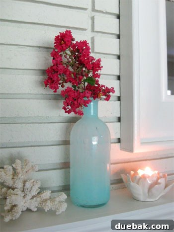 Hot pink crape myrtle branch in a blue glass vase on a living room mantel