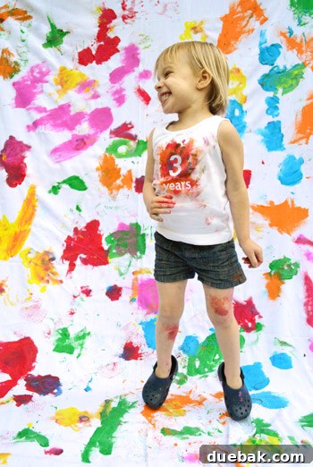 Clara happily sitting on a custom-painted fabric for her third birthday photoshoot