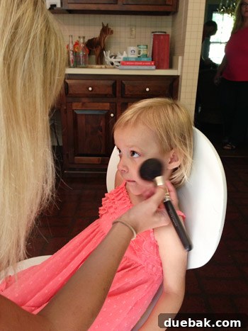 Child happily sitting in a makeup chair with a makeup artist
