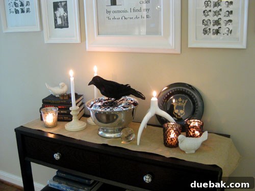 Elegant Thanksgiving console table decor featuring white pumpkins, glittering votives, a rustic cake stand with corks, and stacked cream and brown books, creating a cozy and inviting fall atmosphere.