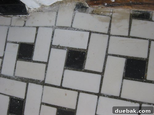 Detail view of stained and uneven bathroom floor tiles, revealing wear and tear