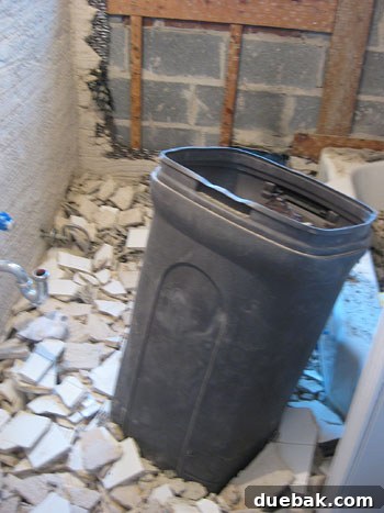 An interior bathroom wall partially demolished, revealing layers of mortar, mesh lath, and wooden studs.