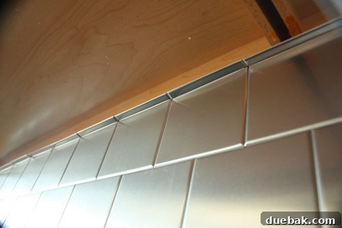 Effortless Elegance: $100 DIY Stainless Stick-On Backsplash 5 Another perspective of the transformed kitchen backsplash, emphasizing the matching stainless steel switchplates and overall cohesive design.