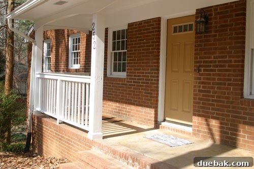 Original rancher home exterior before renovation, showing brick facade and existing porch structure with railings, presenting a typical suburban appearance.