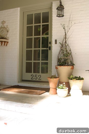 Close-up detailed view of the renovated French Country cottage porch, highlighting the new front door with elegant Emtek hardware, texture-rich seagrass rugs, and refined exterior architectural details, all contributing to the inviting atmosphere.