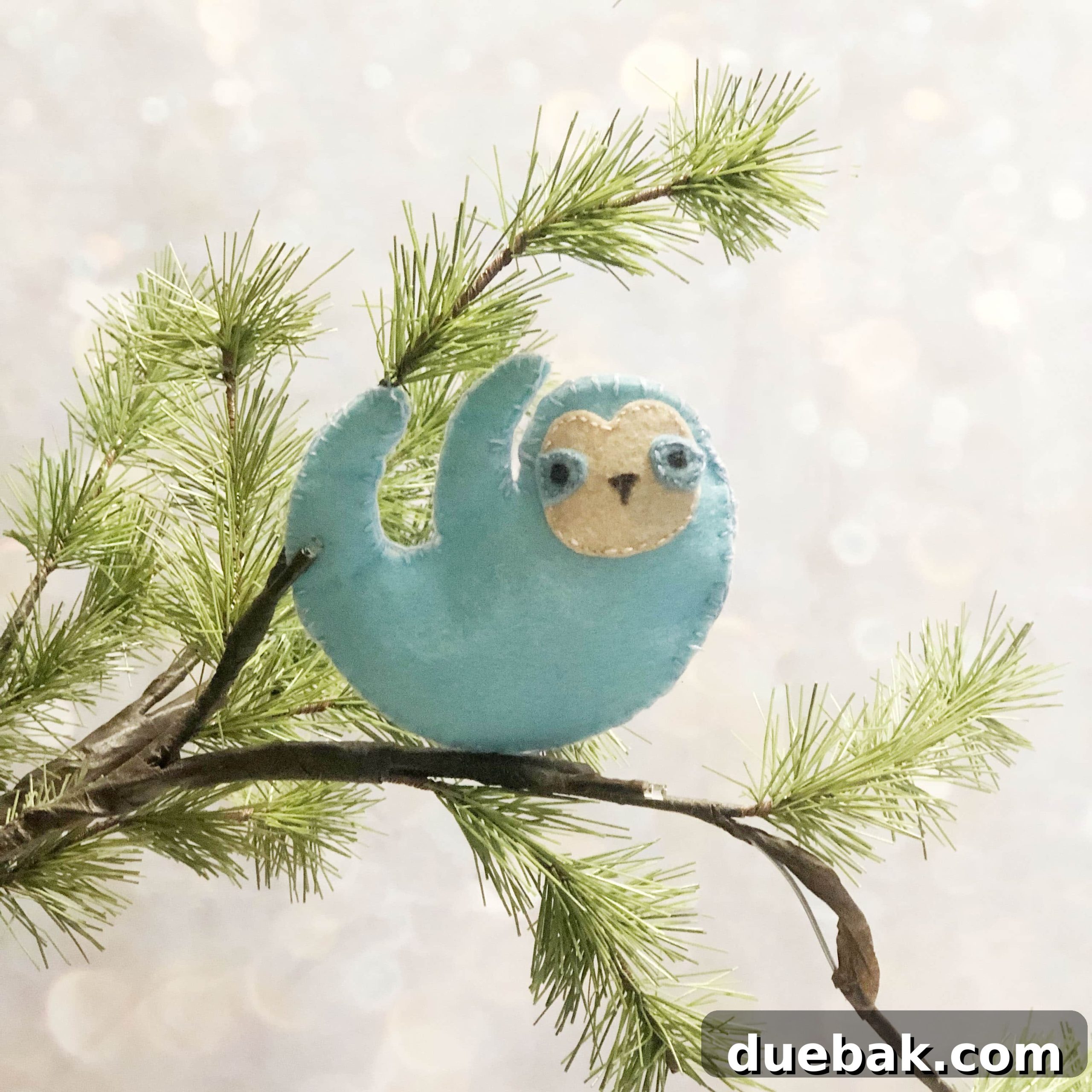 A finished DIY felt sloth ornament hanging on a branch.