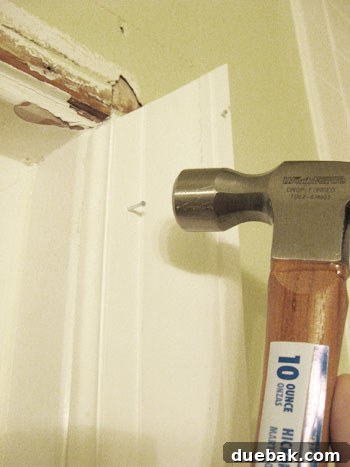Elevate Your Bathroom Renovation with Flawless Baseboard and Trim Installation 7 Hammering a finishing nail partially into a trim piece for initial securement.