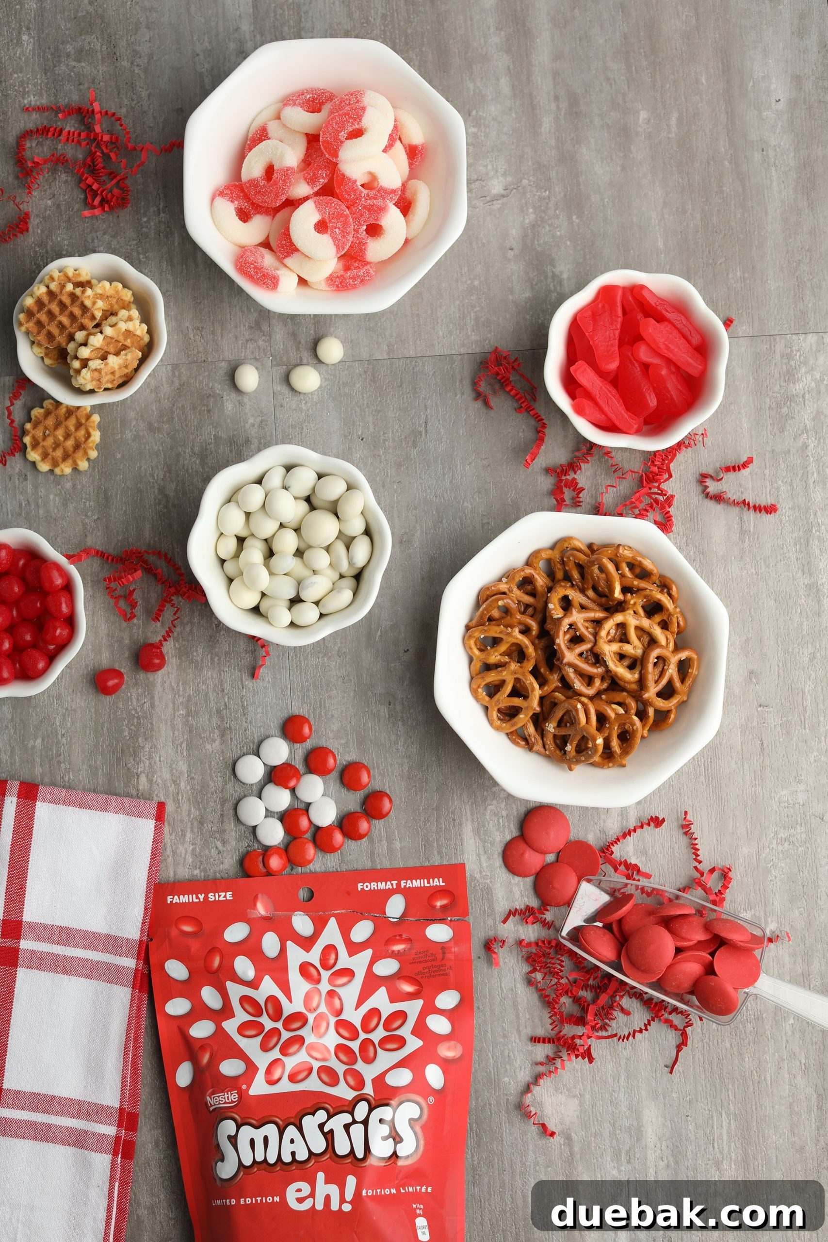 Close-up of Canada Day trail mix ingredients arranged on a white surface, featuring red and white candies, pretzels, and chips