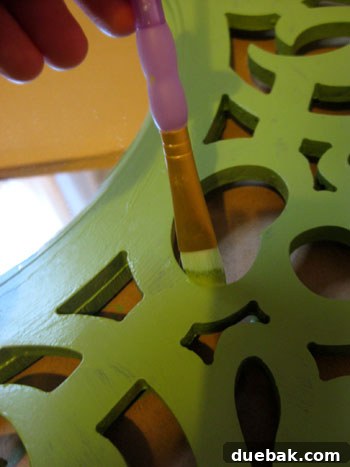 Close-up view of the mirror frame being hand-painted with a small brush in a deep green color, showing careful application on intricate details.