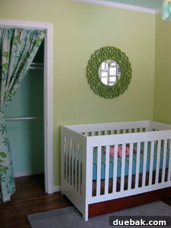 The green painted mirror positioned above a crib in a nursery, with a visible organic aqua crib sheet, highlighting the harmonious color palette.