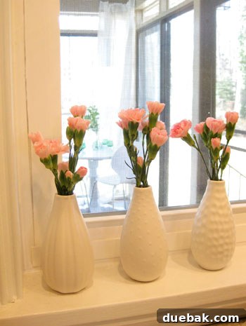 Three small bouquets of pink carnations in budget-friendly Ikea vases on a kitchen window ledge.