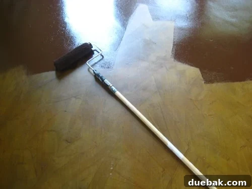 A person expertly painting over a stained concrete floor with a roller, demonstrating an alternative method for achieving a new color and finish.