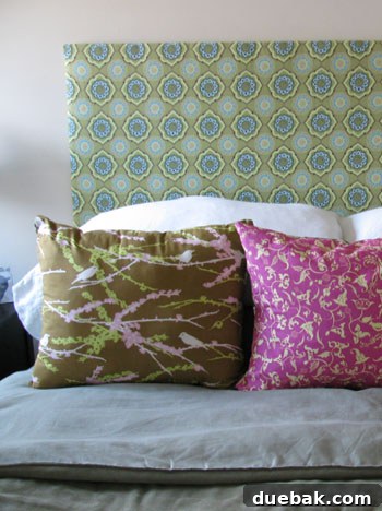 Close-up of Karen's custom upholstered headboard, showcasing the detailed patterned fabric and a collection of matching decorative pillows. A cute Miniature Pinscher dog is nestled on the bed.
