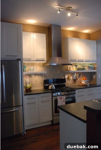 Modern kitchen after renovation with white cabinets, floating shelves, and new appliances.