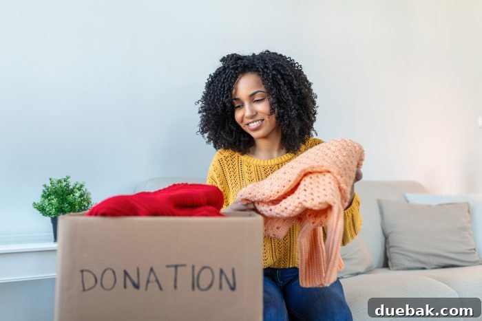 Woman holding cardboard donation box full with clothes. Concept of volunteering work, donation and clothes recycling. A person carefully places folded clothes into a brown cardboard box, ready for donation. This image emphasizes the positive impact of giving away unused items.