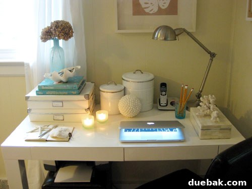 Close-up of beachy desk accessories, including a clam shell, blue cup with pencils, and a notebook.