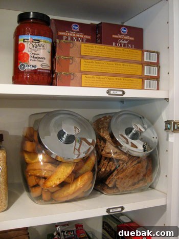 Organized pasta and snack section with glass containers in kitchen cabinet