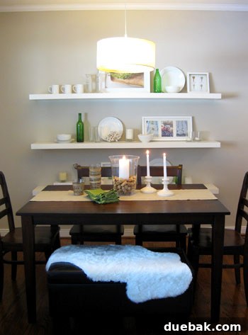 Elegant dining room featuring minimalist white floating Ikea-style shelves above a dark wood dining table with a matching bench seat and a modern drum shade pendant light