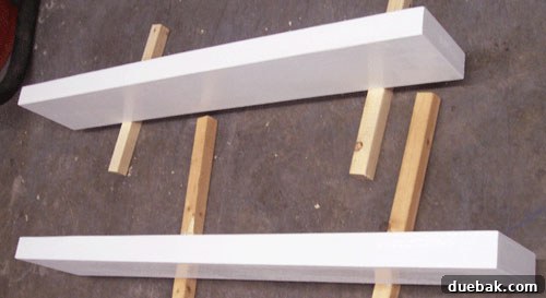 DIY floating shelves propped up and painted pristine white, awaiting installation on the wall
