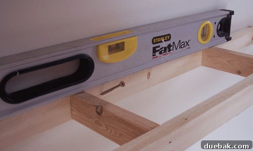 Demonstration of attaching a wooden frame to the wall using a level for precise installation of DIY floating shelves
